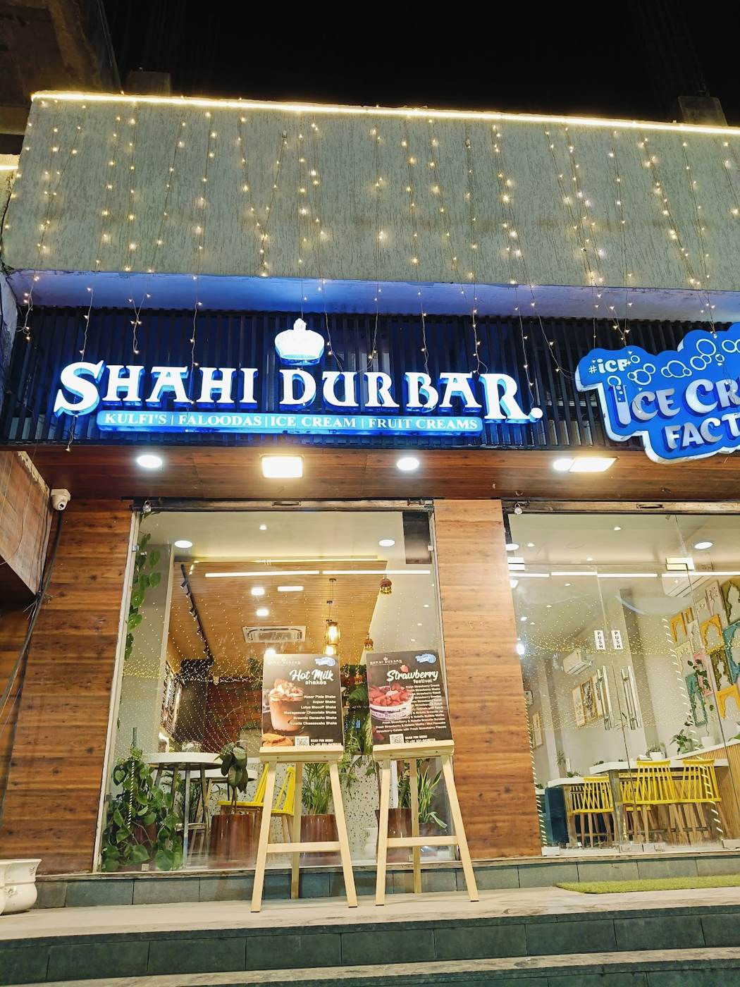 Shahi Durbar storefront at night with its glowing blue sign and yellow chairs